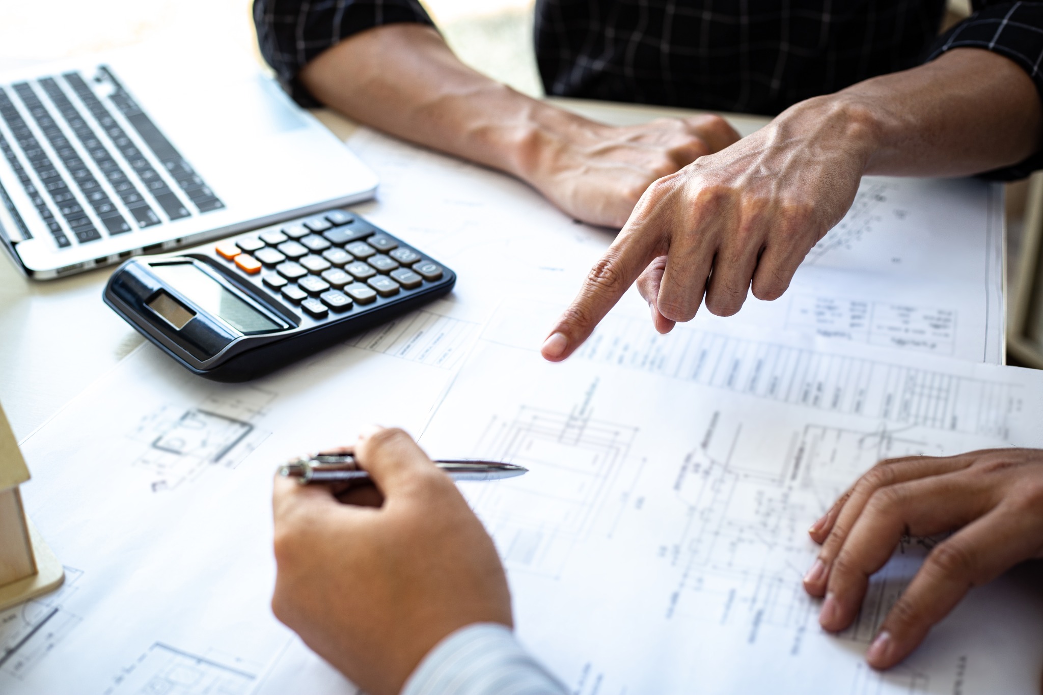 Architectural plans, calculator and laptop used in real estate cost analysis